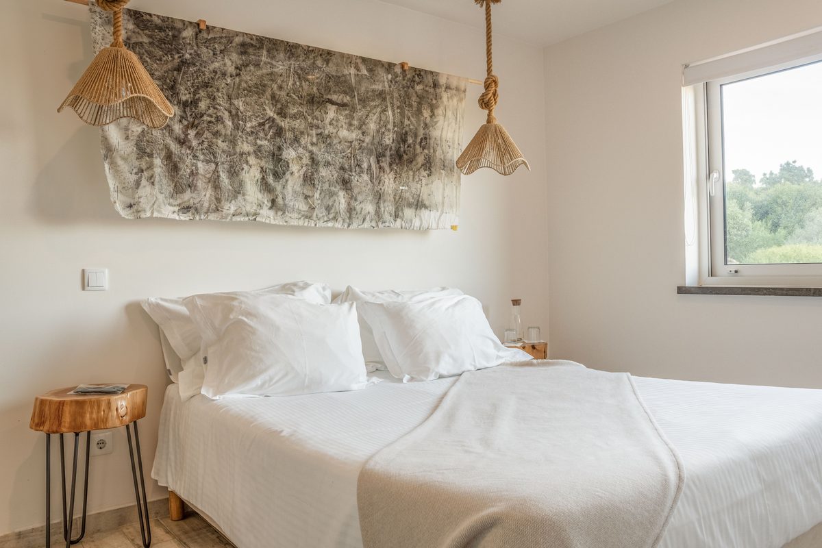 Double bed with a woven hanging above it and a window alongside
