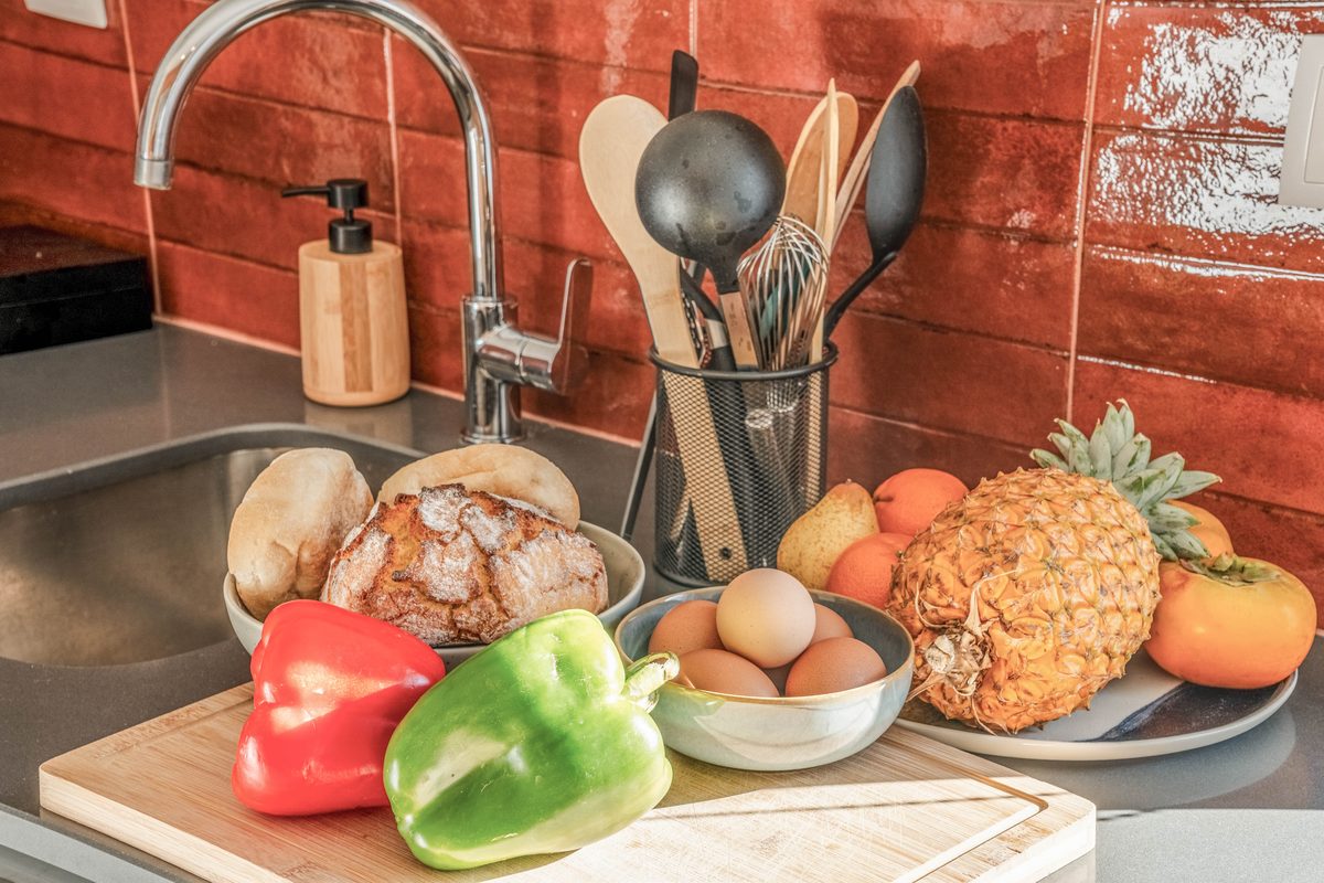 The sink with vegetables, bread and fruit set out on the counter
