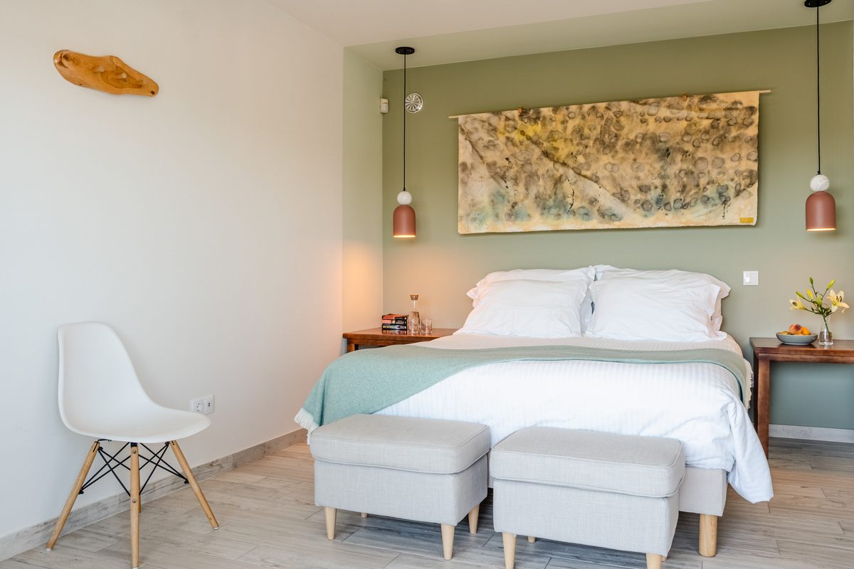 Double bed with ottomans, desk and chair under a framed landscape